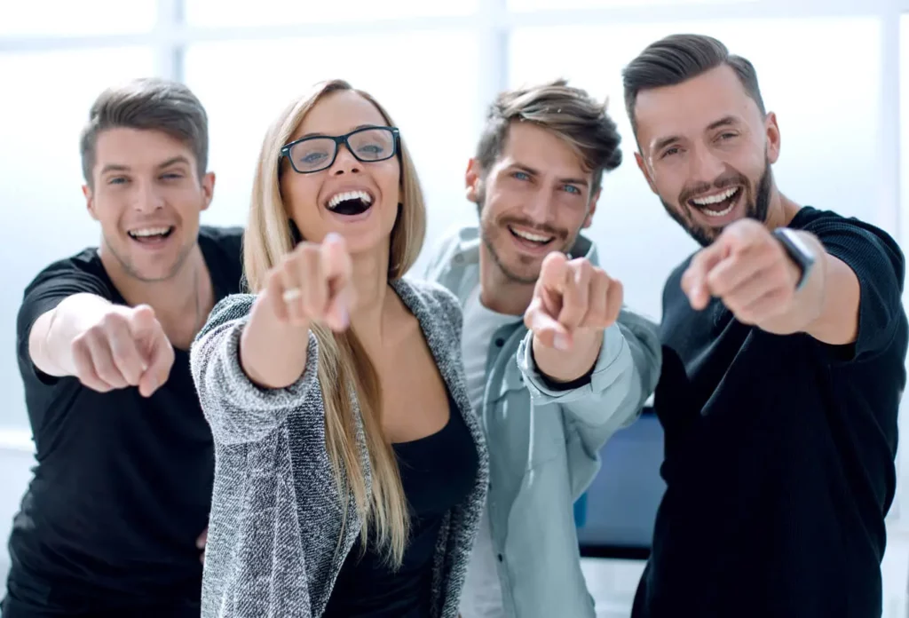 Osteopathie für Erwachsene: Vier lachende Menschen, die mit dem Finger nach vorne zeigen.